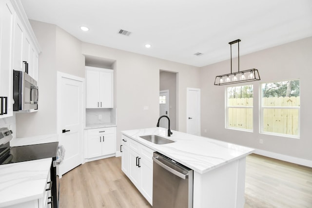 kitchen with white cabinetry, stainless steel appliances, a kitchen island with sink, light stone counters, and sink