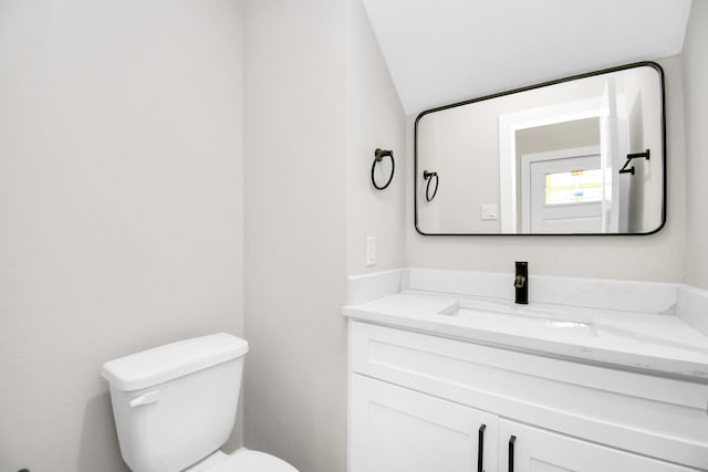 bathroom with toilet, vanity, and lofted ceiling