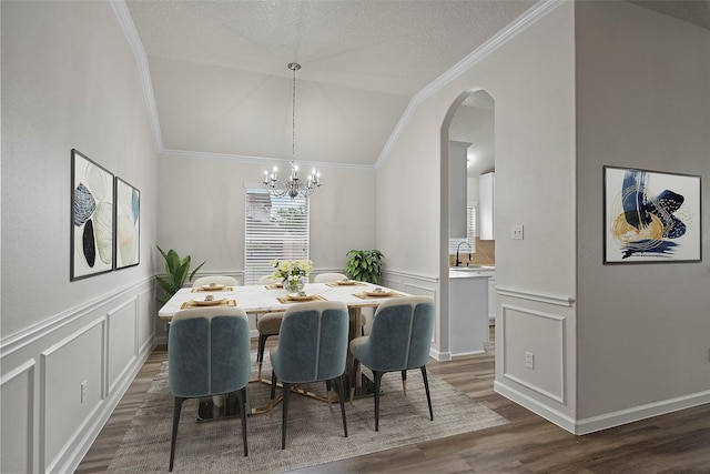 dining space with a textured ceiling, dark wood-type flooring, an inviting chandelier, sink, and vaulted ceiling