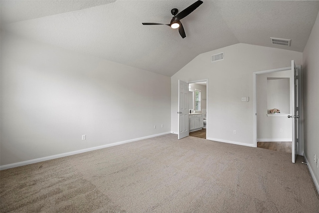 unfurnished bedroom with carpet, a textured ceiling, vaulted ceiling, ceiling fan, and ensuite bathroom