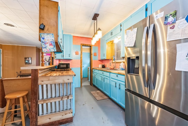 kitchen with blue cabinetry, butcher block counters, sink, decorative light fixtures, and stainless steel fridge