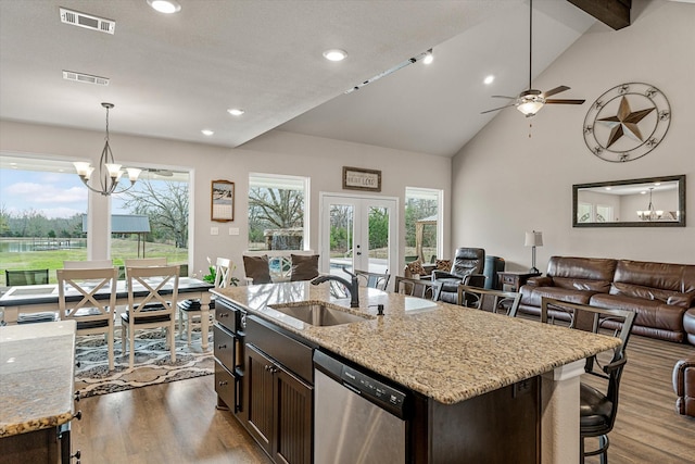 kitchen with a kitchen island with sink, dark brown cabinets, light stone countertops, stainless steel dishwasher, and sink