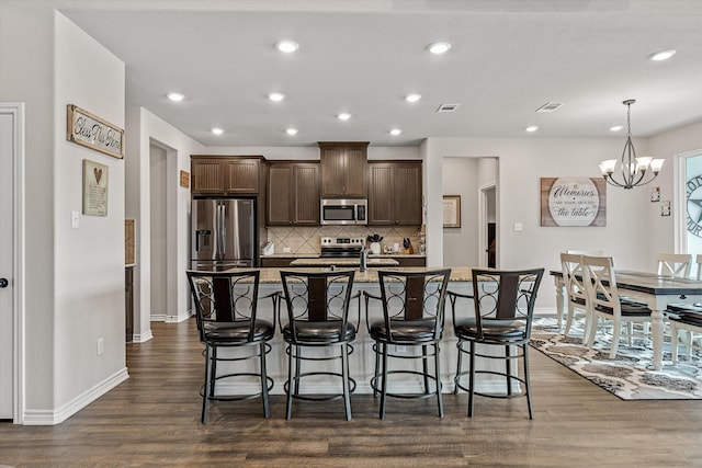 kitchen featuring a center island with sink, stainless steel appliances, dark hardwood / wood-style floors, backsplash, and a notable chandelier