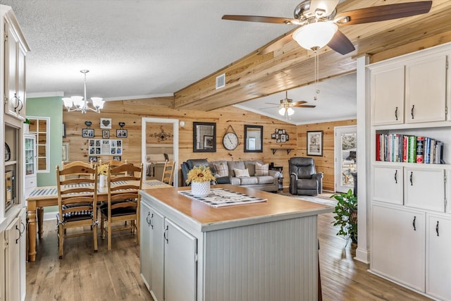 kitchen with wood walls, light wood-type flooring, hanging light fixtures, a kitchen island, and white cabinets