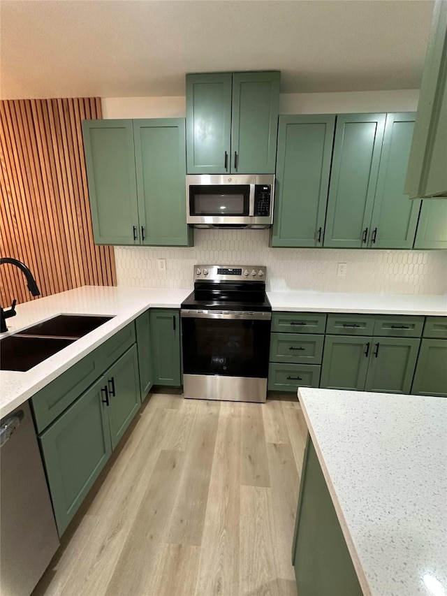 kitchen featuring light hardwood / wood-style floors, decorative backsplash, sink, appliances with stainless steel finishes, and green cabinetry