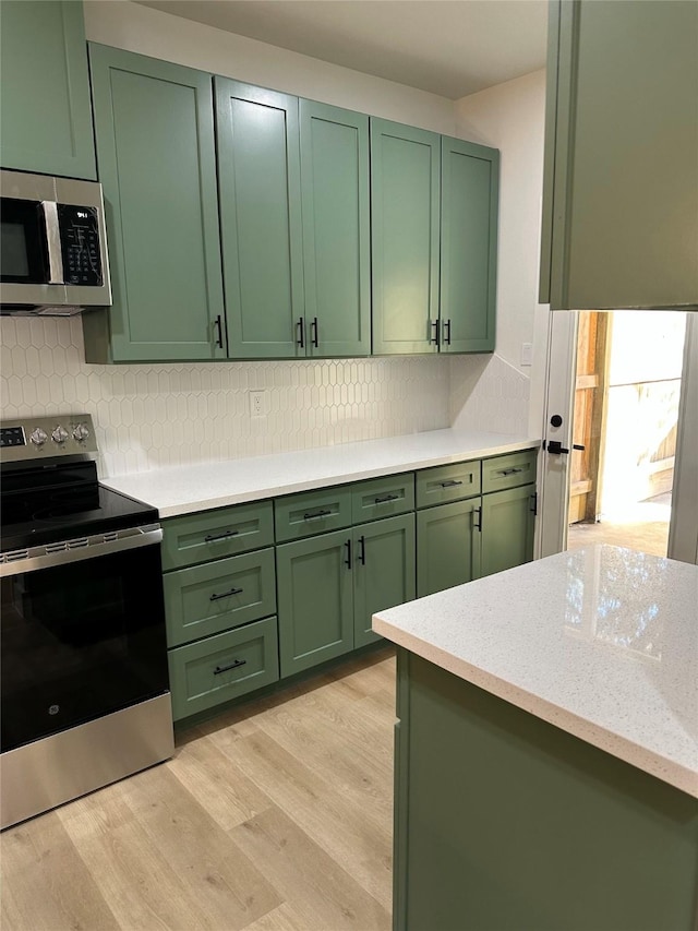 kitchen with light wood-type flooring, decorative backsplash, appliances with stainless steel finishes, and green cabinetry