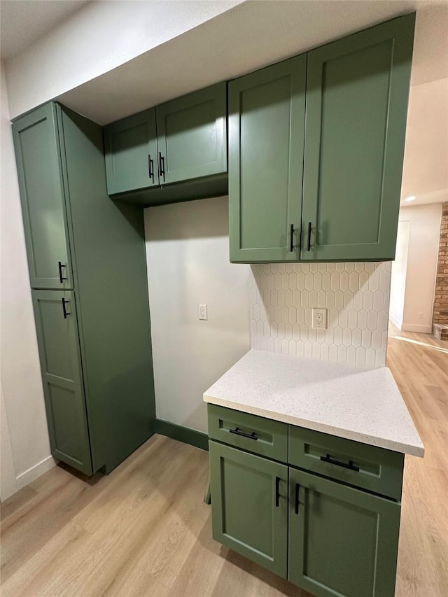 kitchen with light wood-type flooring, green cabinets, decorative backsplash, and light stone counters