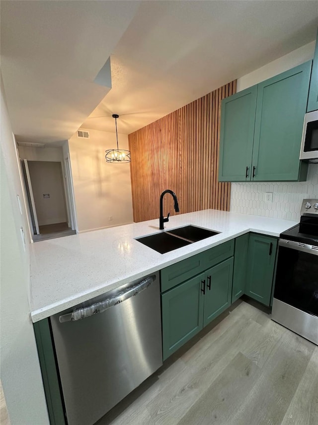 kitchen with backsplash, pendant lighting, sink, green cabinets, and stainless steel appliances