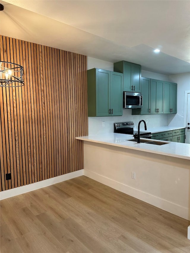 kitchen with stainless steel appliances, tasteful backsplash, sink, kitchen peninsula, and light hardwood / wood-style flooring