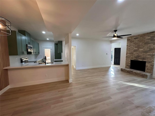 unfurnished living room featuring ceiling fan, sink, light hardwood / wood-style flooring, and a fireplace