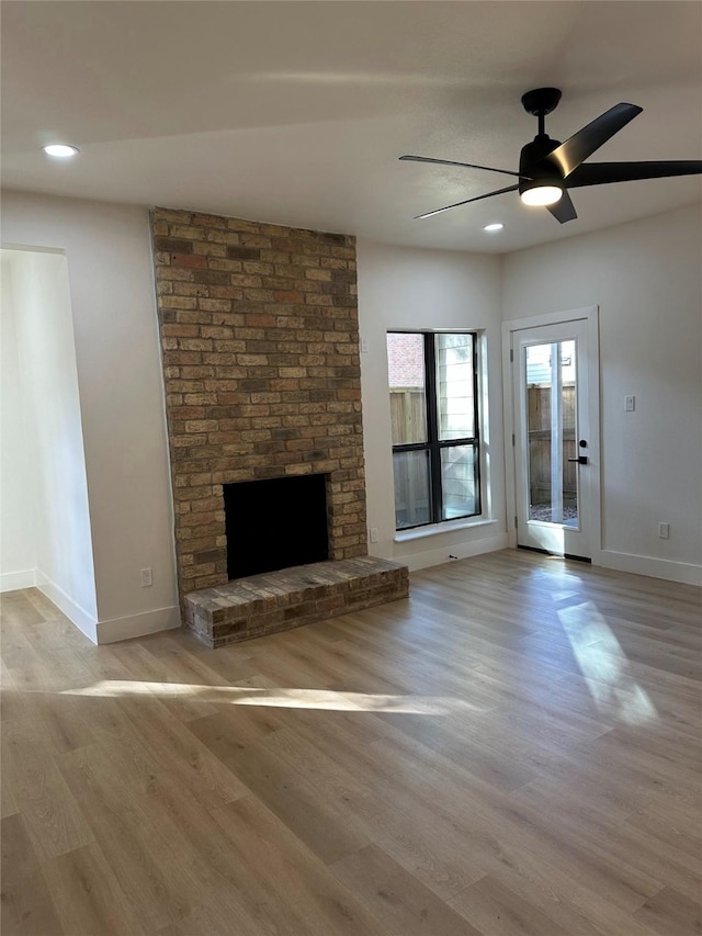 unfurnished living room with ceiling fan, a fireplace, and light hardwood / wood-style floors