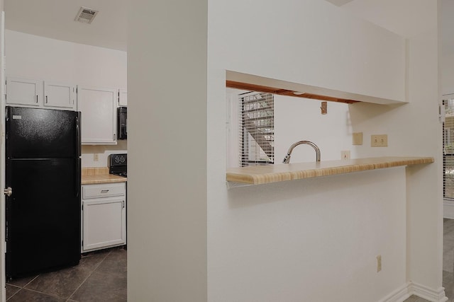 kitchen with dark tile patterned floors, black refrigerator, white cabinetry, sink, and kitchen peninsula