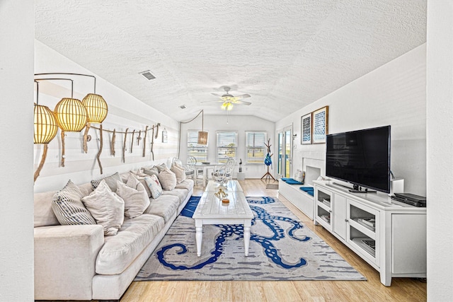 living room with vaulted ceiling, ceiling fan, a textured ceiling, and light wood-type flooring