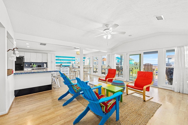 interior space with a textured ceiling, ceiling fan, lofted ceiling, and light wood-type flooring