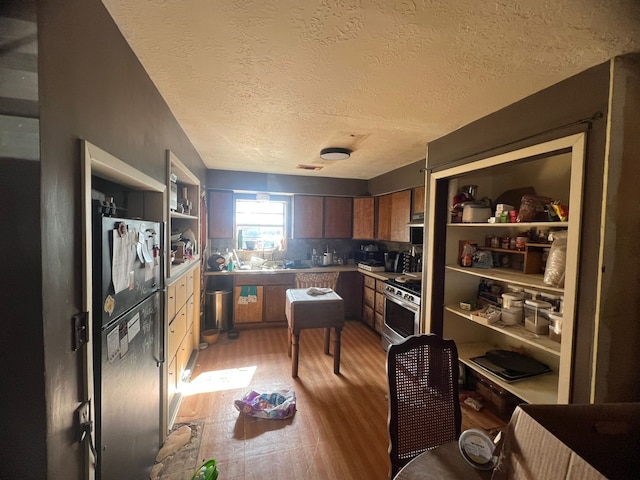 kitchen featuring refrigerator, gas range, a textured ceiling, and light hardwood / wood-style flooring