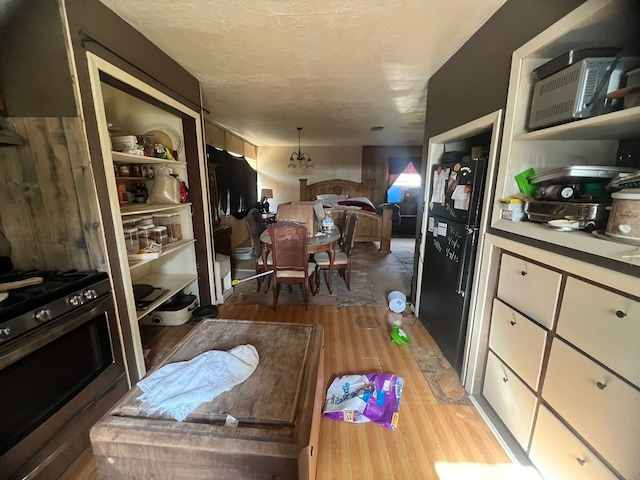 kitchen with stainless steel gas range, black refrigerator, built in shelves, light hardwood / wood-style floors, and hanging light fixtures