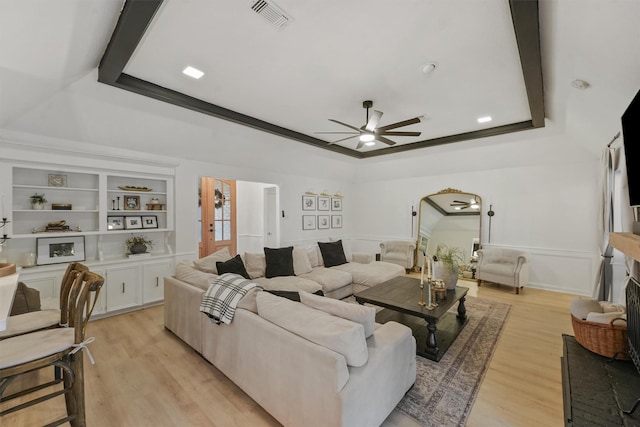 living room with ornamental molding, built in features, light hardwood / wood-style floors, and a raised ceiling