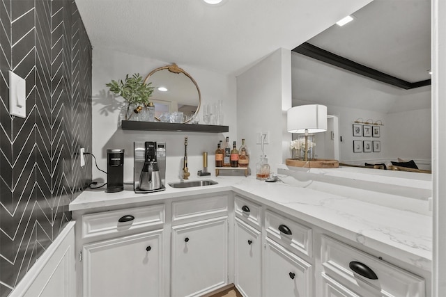 bar with white cabinetry, sink, light stone counters, and crown molding