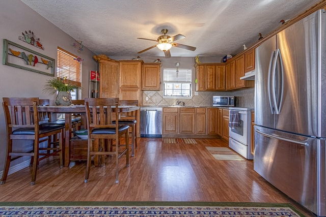 kitchen featuring ceiling fan, backsplash, hardwood / wood-style flooring, appliances with stainless steel finishes, and a textured ceiling