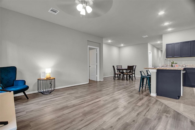 kitchen with a breakfast bar area, ceiling fan, light stone countertops, light hardwood / wood-style flooring, and sink