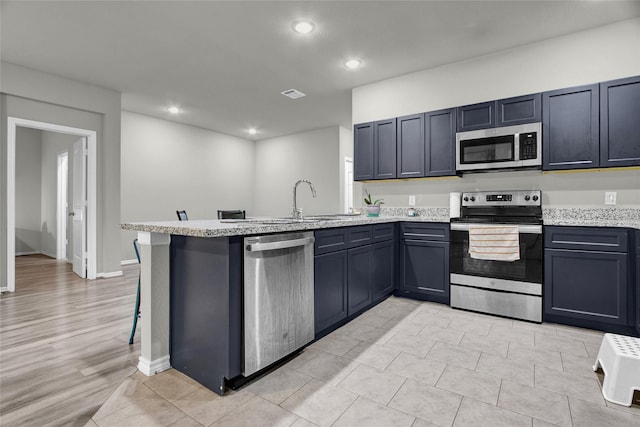 kitchen featuring kitchen peninsula, a kitchen bar, appliances with stainless steel finishes, light tile patterned floors, and light stone counters