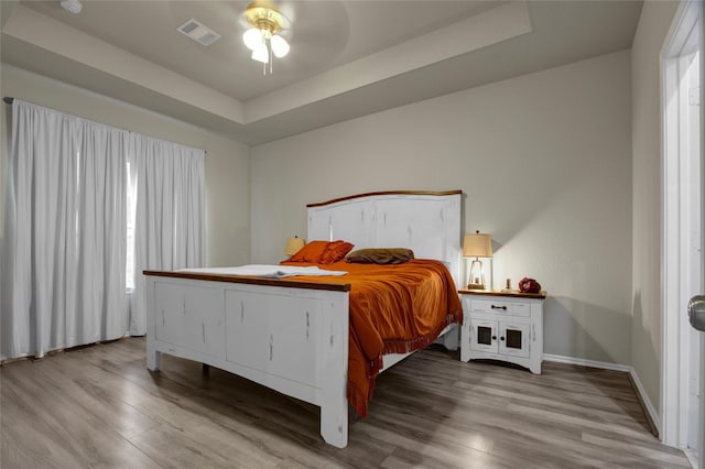 bedroom featuring a raised ceiling, ceiling fan, and light hardwood / wood-style flooring