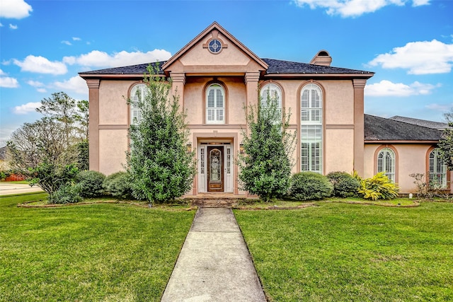 view of front of property featuring stucco siding, a chimney, and a front yard