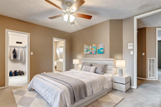 bedroom with ceiling fan, light colored carpet, a closet, and ensuite bath