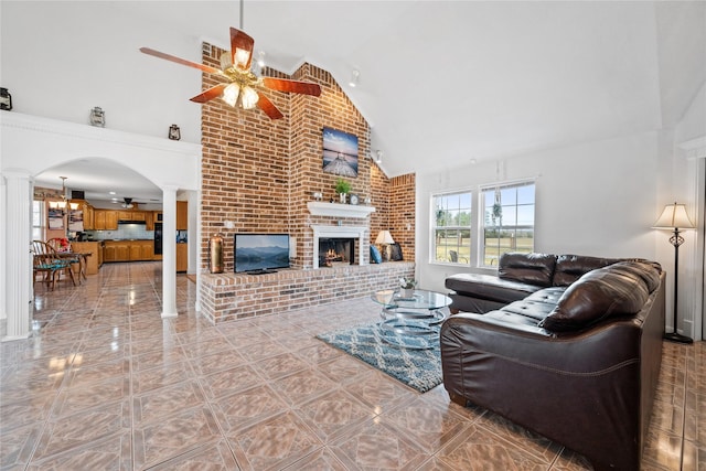 living room featuring ceiling fan with notable chandelier, brick wall, high vaulted ceiling, and a fireplace