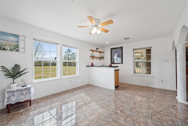 unfurnished living room featuring ceiling fan and decorative columns