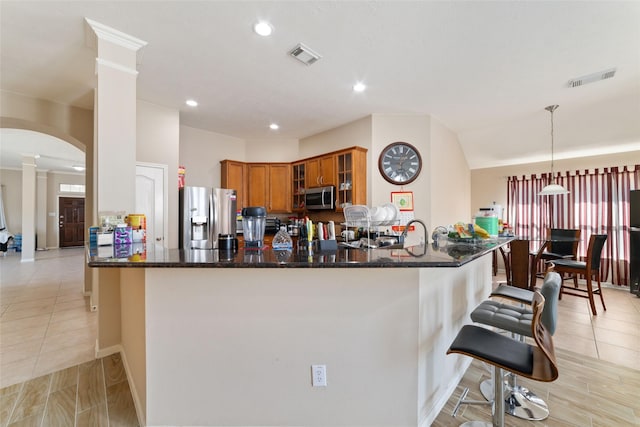 kitchen with decorative light fixtures, appliances with stainless steel finishes, kitchen peninsula, dark stone counters, and decorative columns