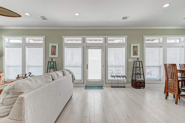 living room with light wood-type flooring, ornamental molding, and plenty of natural light