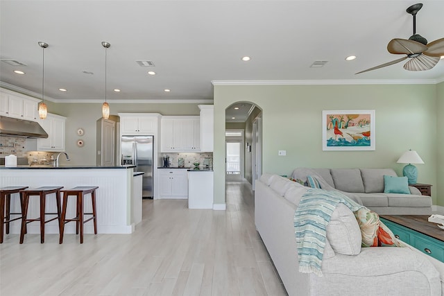 living room featuring light wood-type flooring, ceiling fan, ornamental molding, and sink