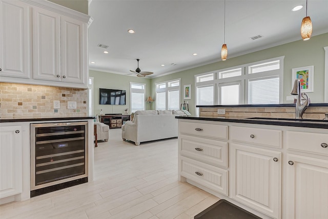 kitchen featuring ceiling fan, beverage cooler, pendant lighting, white cabinets, and sink