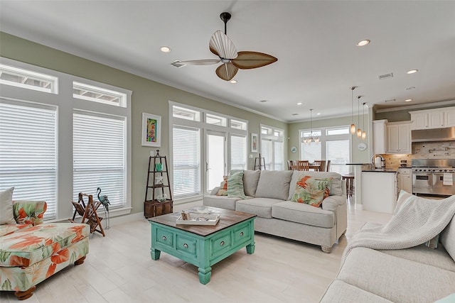 living room featuring ceiling fan, ornamental molding, and sink