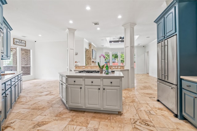 kitchen with blue cabinets, appliances with stainless steel finishes, a kitchen island, ceiling fan, and decorative columns