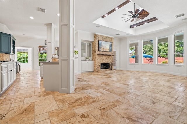 unfurnished living room featuring crown molding, ceiling fan, a tray ceiling, and a large fireplace