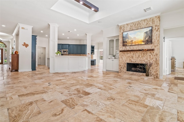 unfurnished living room featuring a large fireplace, ornamental molding, and ornate columns