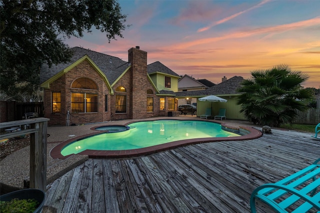 pool at dusk featuring an in ground hot tub, a deck, and a patio area