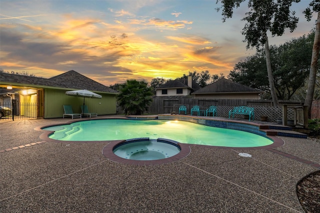 pool at dusk featuring a patio and an in ground hot tub