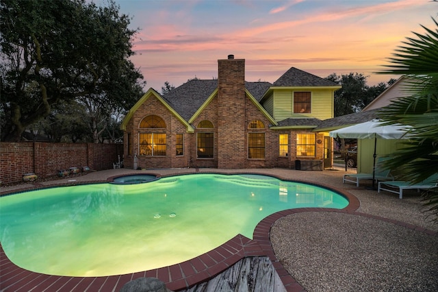 pool at dusk featuring an in ground hot tub and a patio