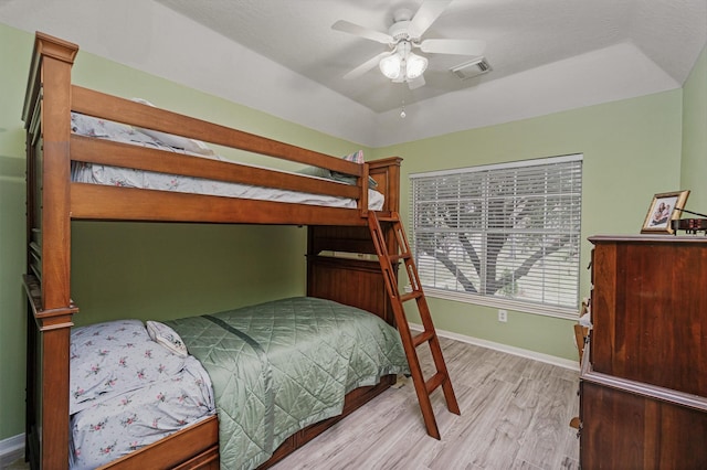 bedroom with ceiling fan, a raised ceiling, and light wood-type flooring