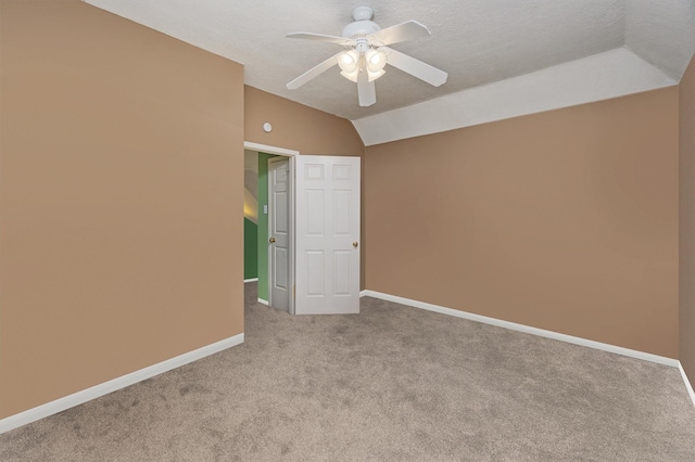 carpeted spare room with vaulted ceiling, a textured ceiling, and ceiling fan