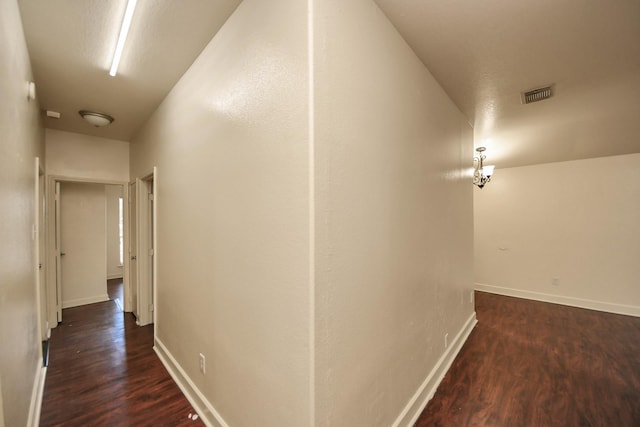 hallway with dark hardwood / wood-style floors and a notable chandelier