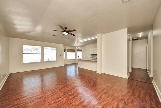 unfurnished living room featuring lofted ceiling, dark hardwood / wood-style flooring, and ceiling fan with notable chandelier