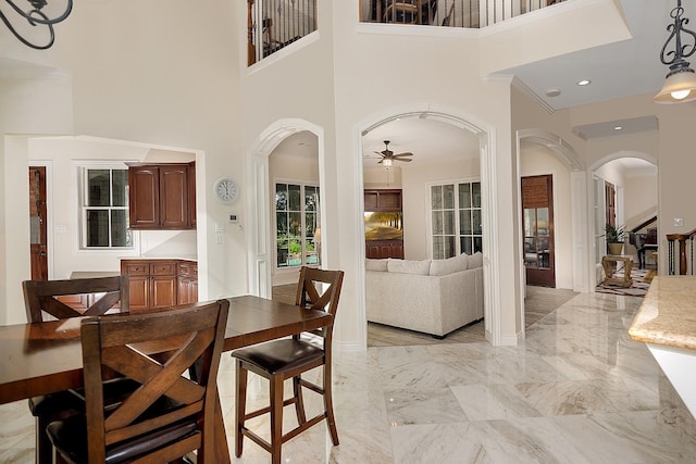 dining space with ceiling fan, a towering ceiling, and crown molding