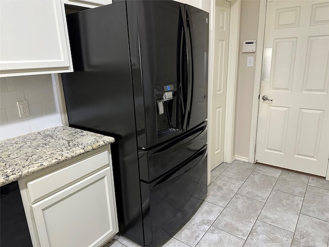 kitchen with light tile patterned floors, backsplash, black fridge with ice dispenser, light stone countertops, and white cabinets