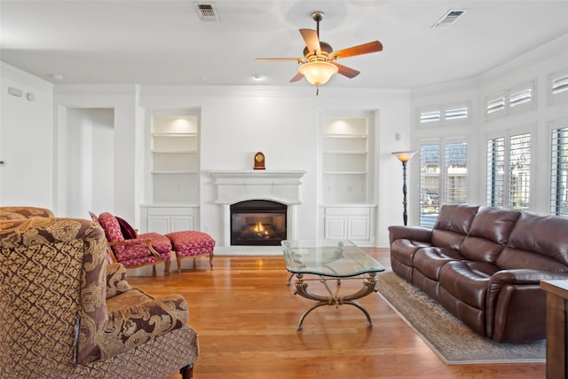 living room featuring ceiling fan, built in shelves, and light wood-type flooring