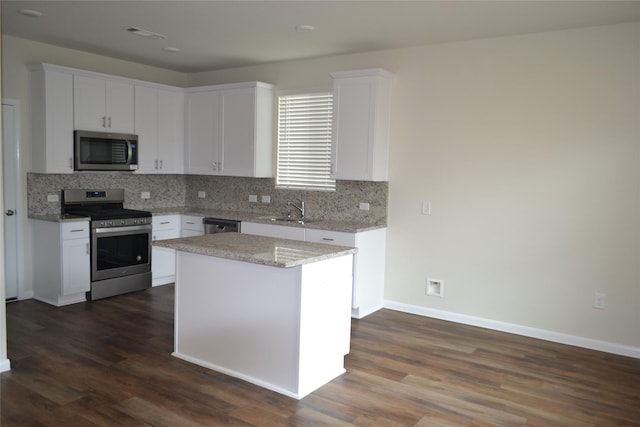 kitchen with white cabinets, a kitchen island, stainless steel appliances, sink, and light stone counters