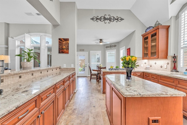 kitchen featuring light stone counters, kitchen peninsula, a kitchen island, ceiling fan, and decorative backsplash